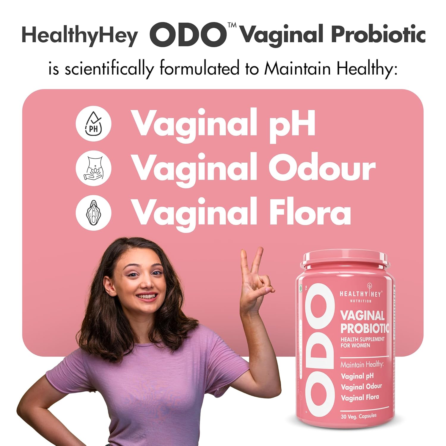 Woman making a peace sign next to a container of HealthyHey ODO Vaginal Probiotic on a pink background