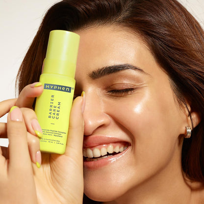 Woman holding a green bottle of Hyphen Barrier Bare Cream close to her face.