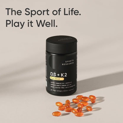 Black supplement bottle labeled 'D3 + K2' with orange capsules on a beige background, featuring the text 'The Sport of Life. Play it Well.