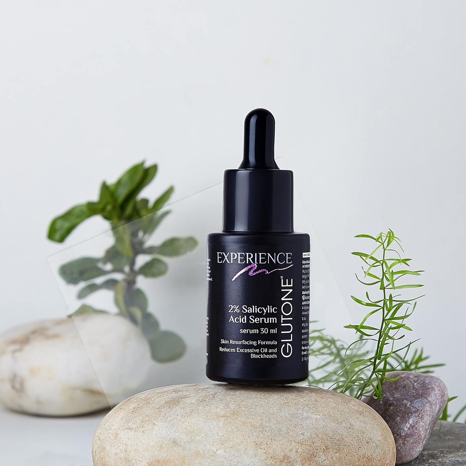 Glutone 2% Salicylic Acid Serum bottle with dropper on a stone surface with plants in the background