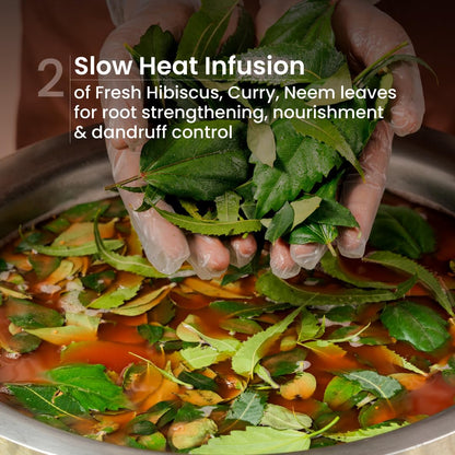 Person adding fresh hibiscus, curry, and neem leaves into a pot for slow heat infusion.