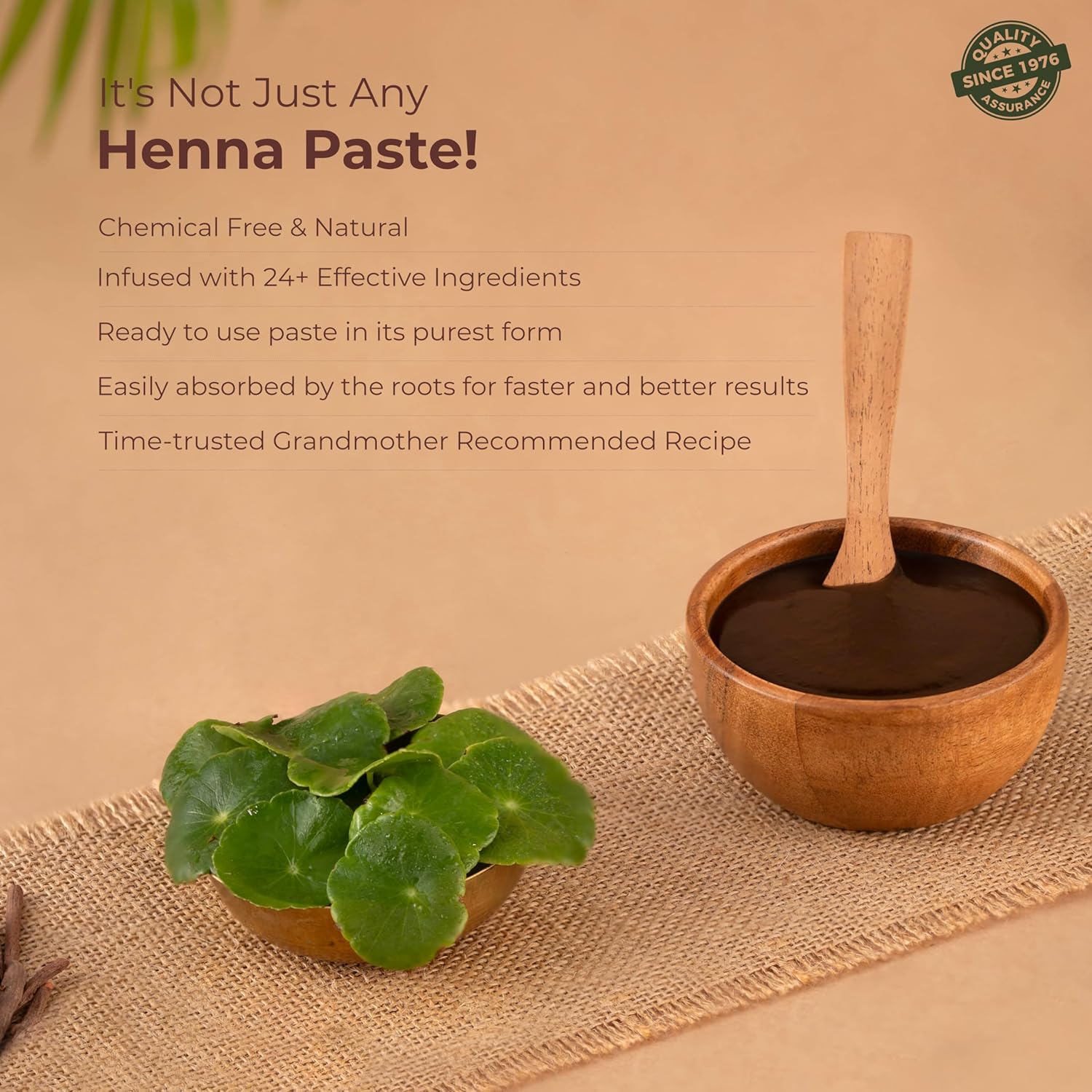 Henna paste in a wooden bowl with a wooden spoon, surrounded by henna leaves on a beige background.
