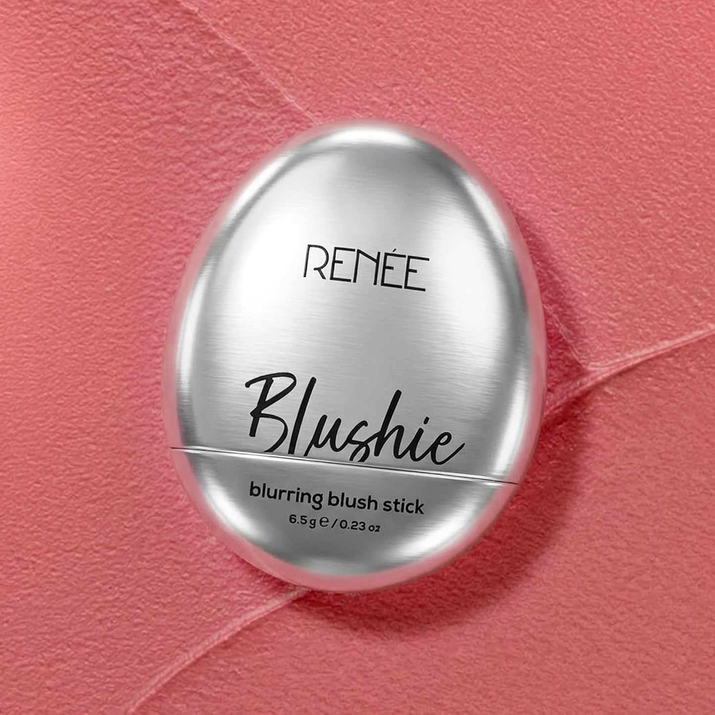 Silver blush stick container labeled 'Blushie' on a pink textured background