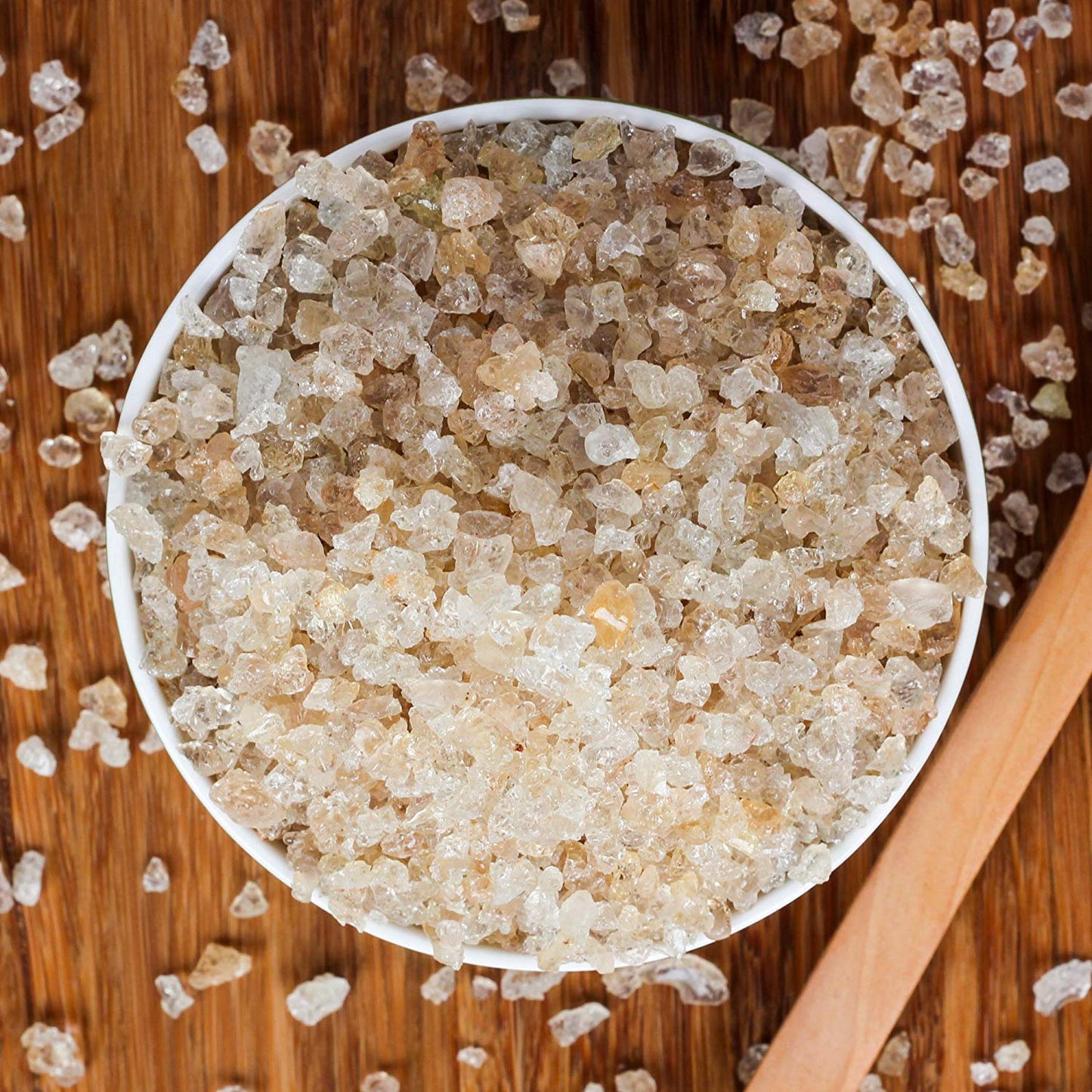 Close-up of a bowl filled with brown sugar crystals on a wooden surface.
