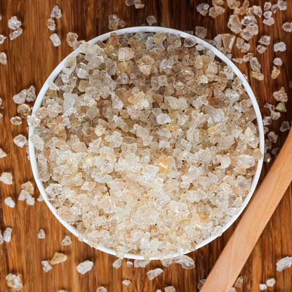 Close-up of a bowl filled with brown sugar crystals on a wooden surface.