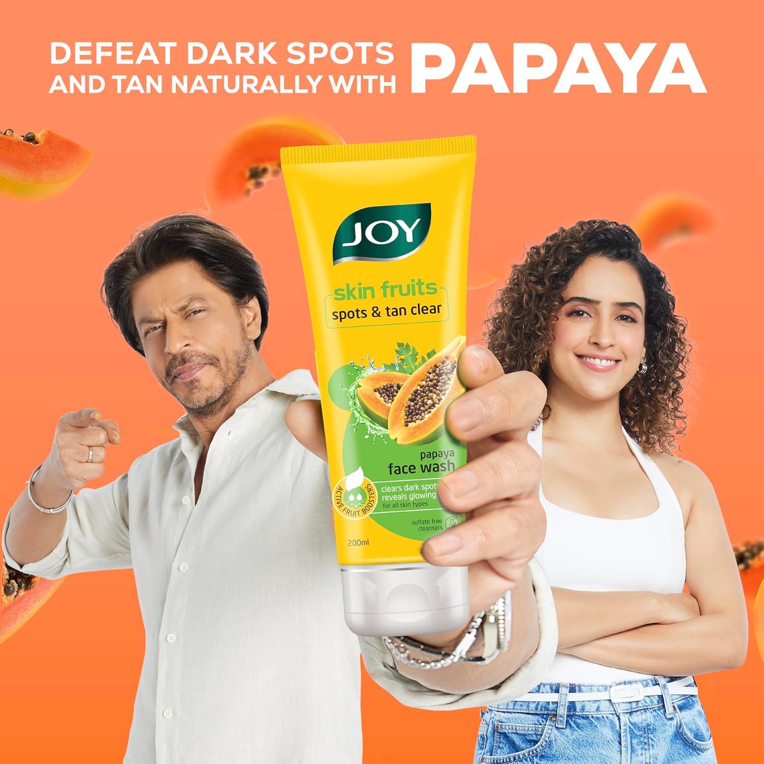 Two people holding a tube of 'JOY skin fruits' papaya face wash against an orange background.