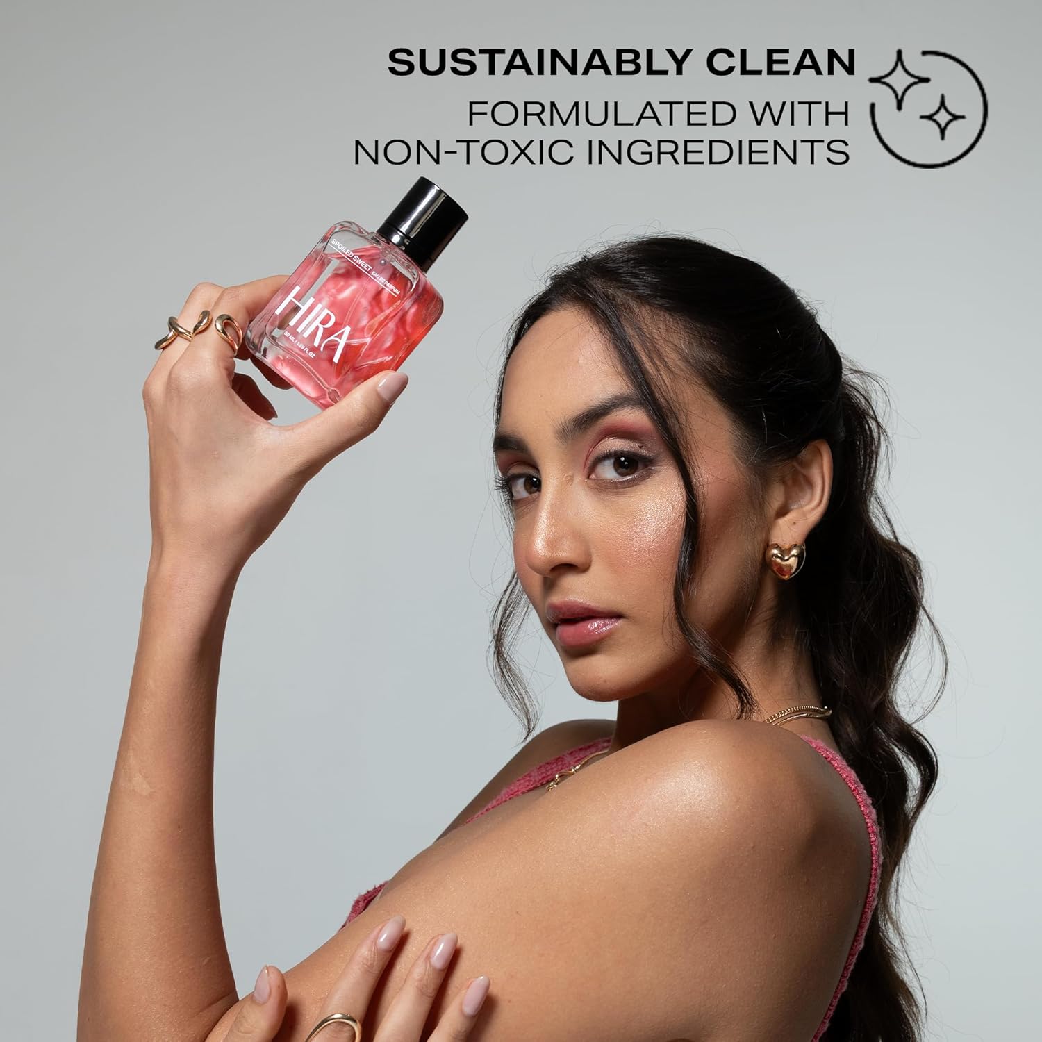 Woman holding a pink bottle labeled 'Hira' with text about sustainability and non-toxic ingredients on a gray background.