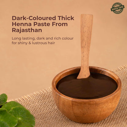 Wooden bowl with dark henna paste and a wooden spoon on a beige background, with text about henna paste from Rajasthan.