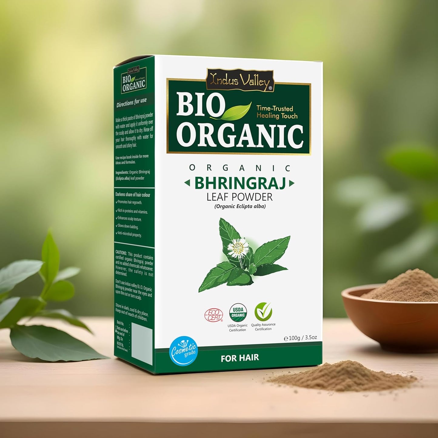 Box of Bio Organic Bhringraj Leaf Powder on a wooden surface with greenery in the background