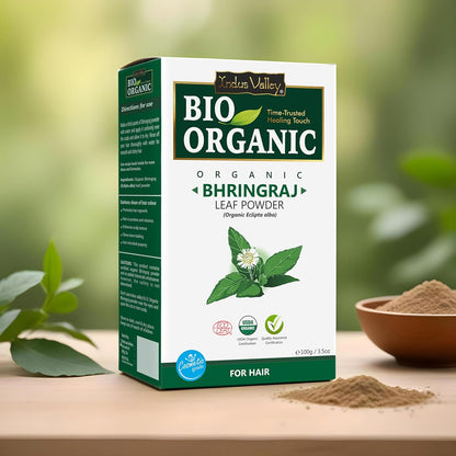 Box of Bio Organic Bhringraj Leaf Powder on a wooden surface with greenery in the background