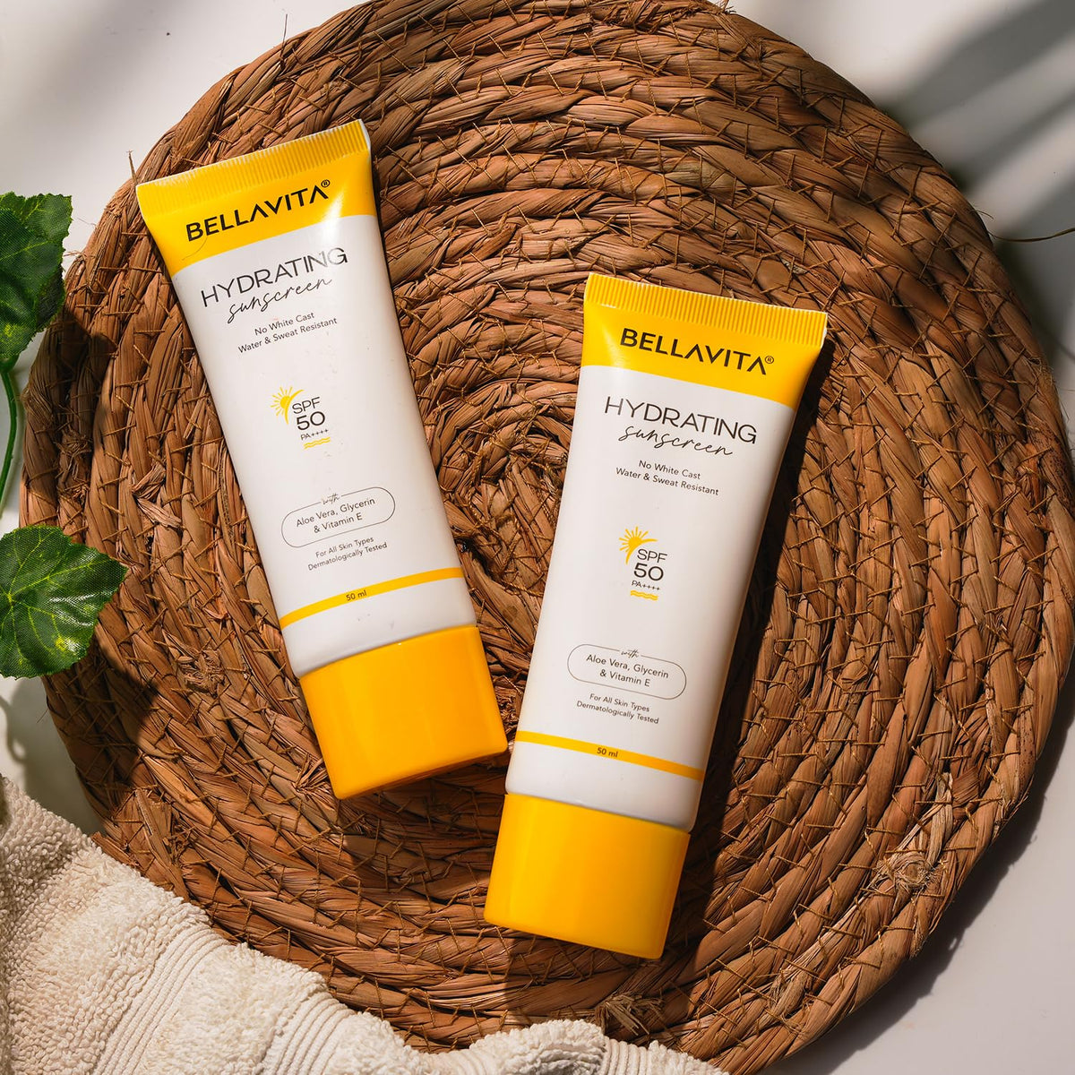 Two bottles of Bellavita hydrating sunscreens on a woven mat.
