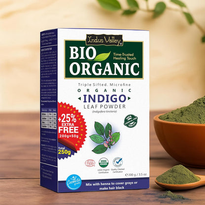 Box of Indus Valley Bio Organic Indigo Leaf Powder with a bowl and spoon of powder on a wooden surface.
