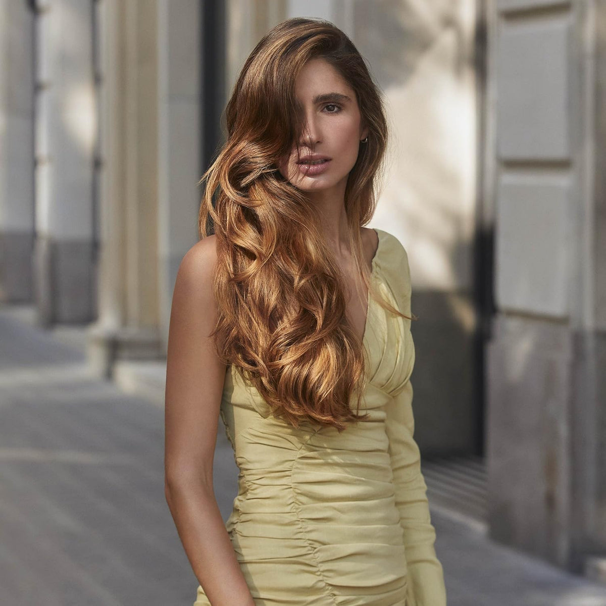 Woman in a yellow dress with long, wavy hair standing outdoors.