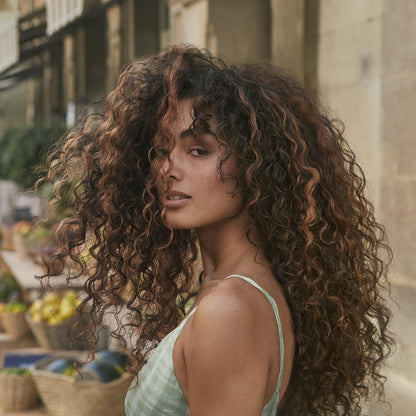 Woman with curly hair standing outdoors with a market in the background