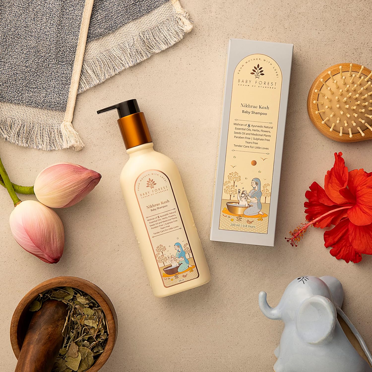 Baby shampoo bottle with packaging, flowers, and a mortar on a beige surface