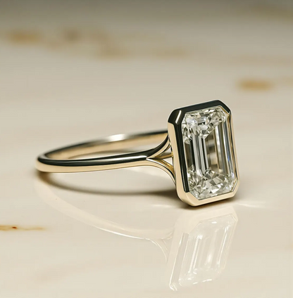 Diamond ring with emerald-cut gemstone on a reflective surface