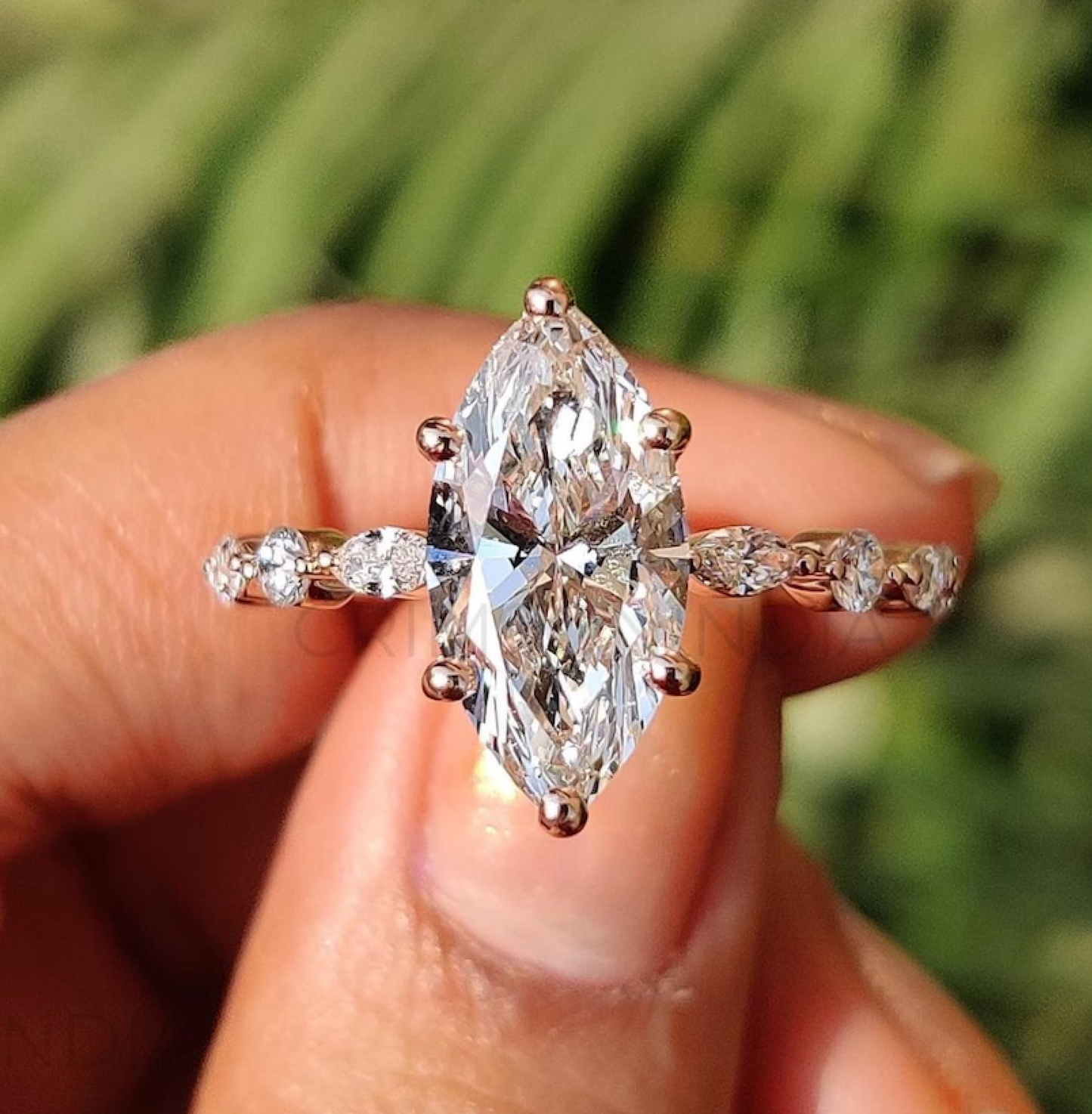 Gold ring with a large pear-shaped diamond held in a hand against a blurred green background