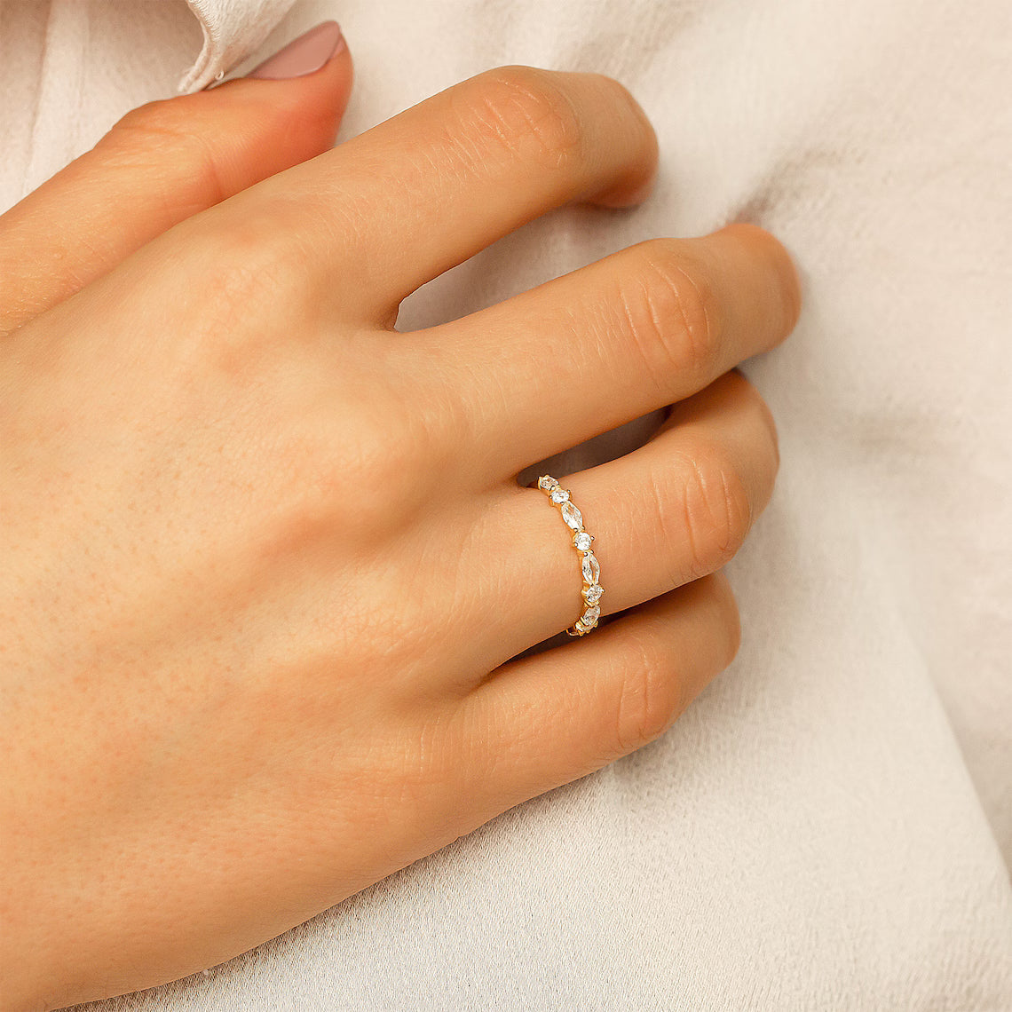 Hand wearing a delicate gold ring with small stones on a light background