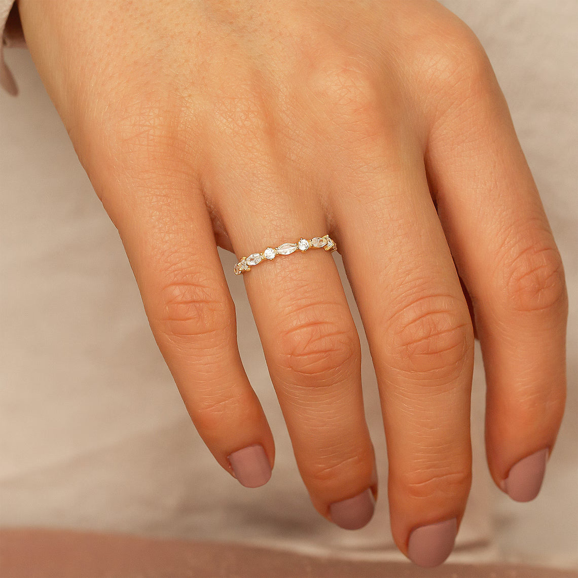 Close-up of a hand wearing a gold ring with a beige background