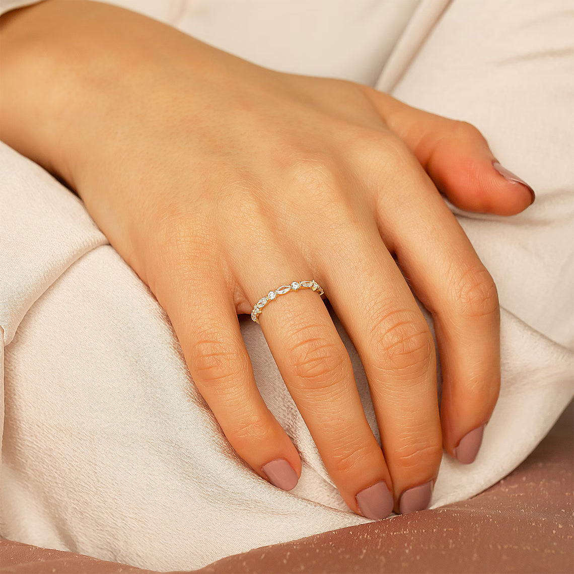 Close-up of a hand wearing a delicate ring on a soft fabric background
