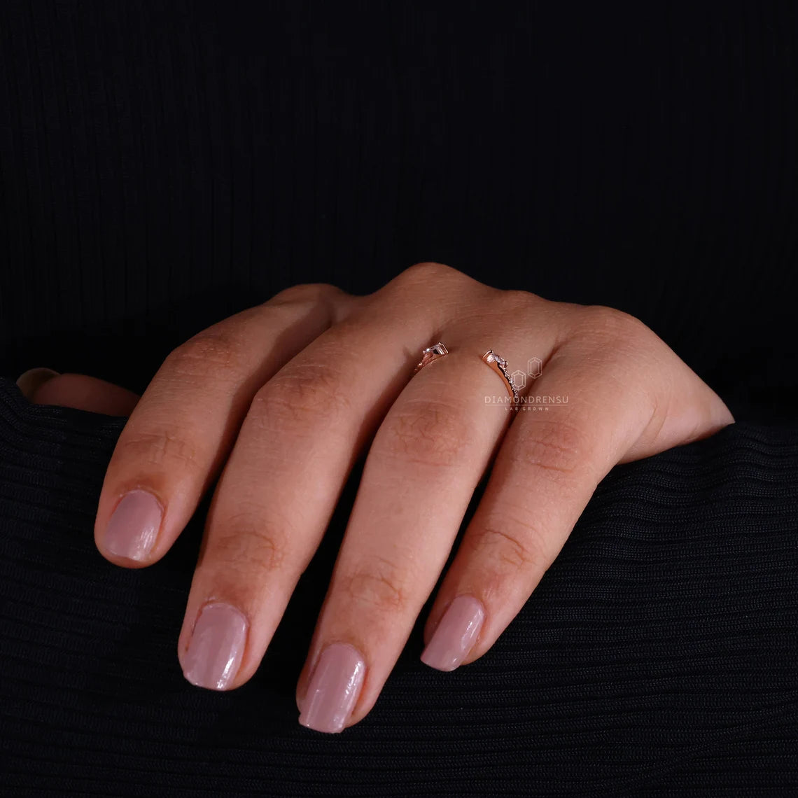 Hand with pink nail polish wearing a ring on a black background