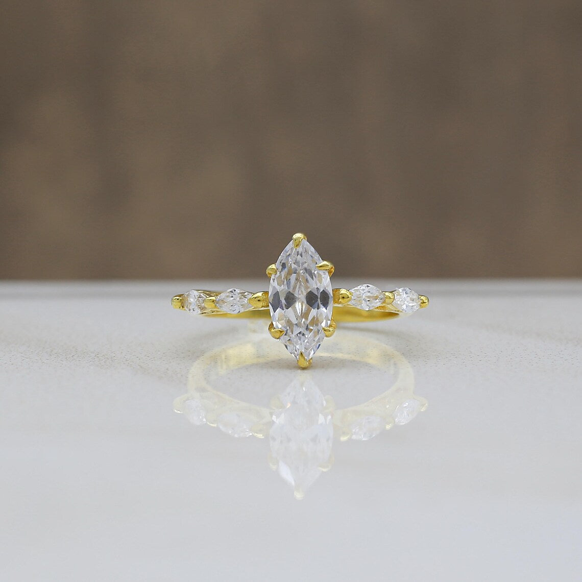 Gold ring with a large central diamond and smaller side diamonds on a reflective surface.