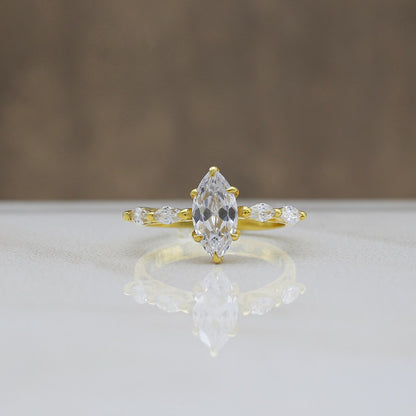 Gold ring with a large central diamond and smaller side diamonds on a reflective surface.