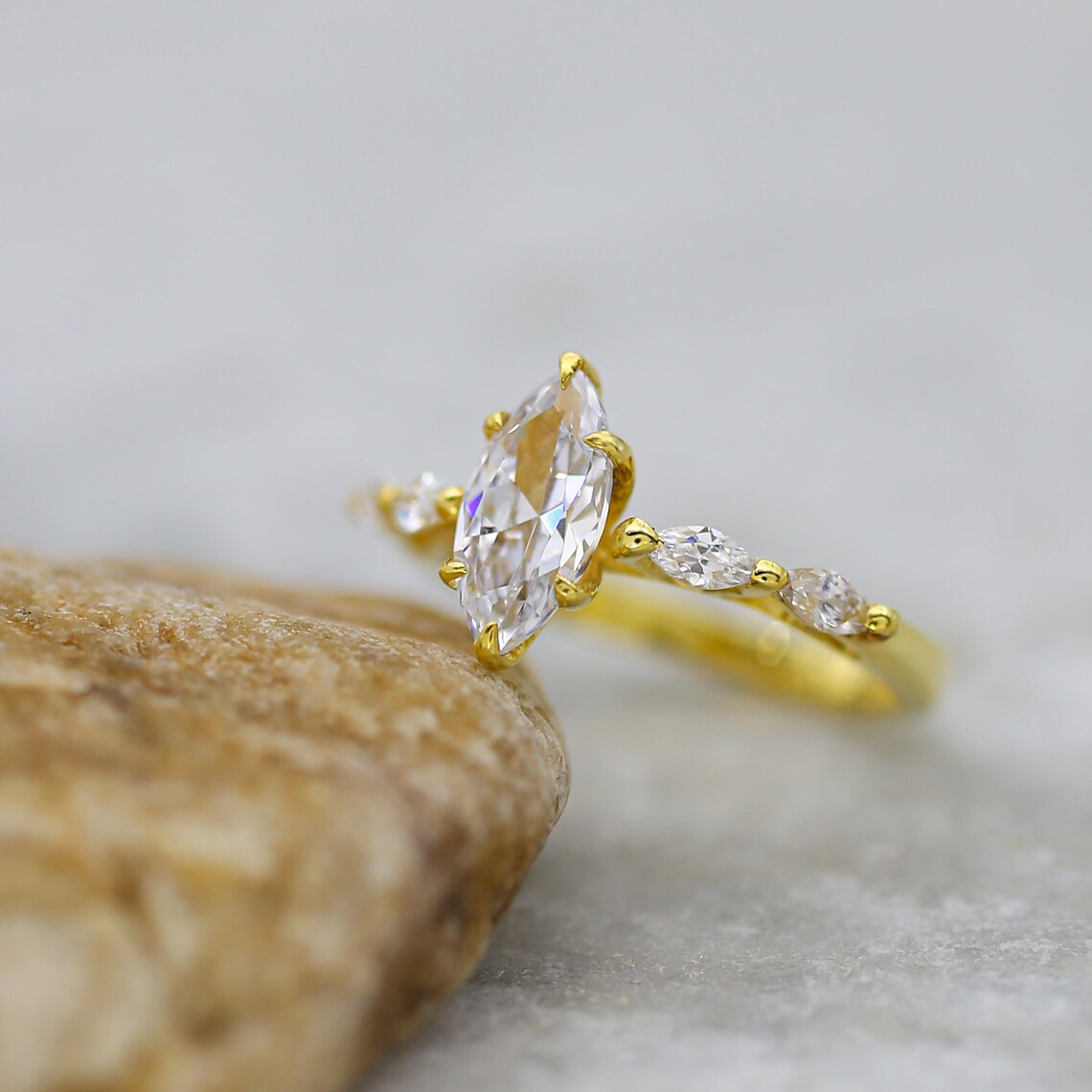 Gold ring with a large marquise-shaped diamond and smaller diamonds on a stone surface