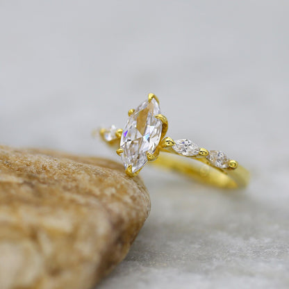 Gold ring with a large marquise-shaped diamond and smaller diamonds on a stone surface