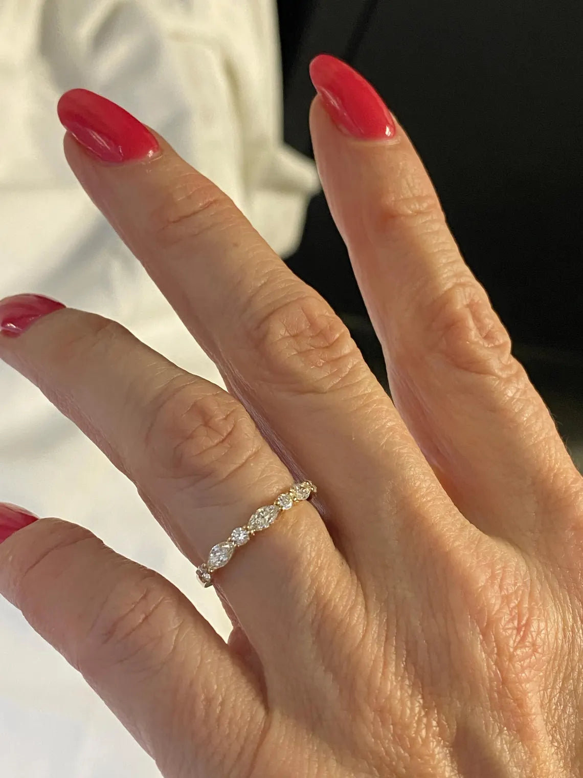 Hand wearing a diamond ring with red nail polish on a blurred background