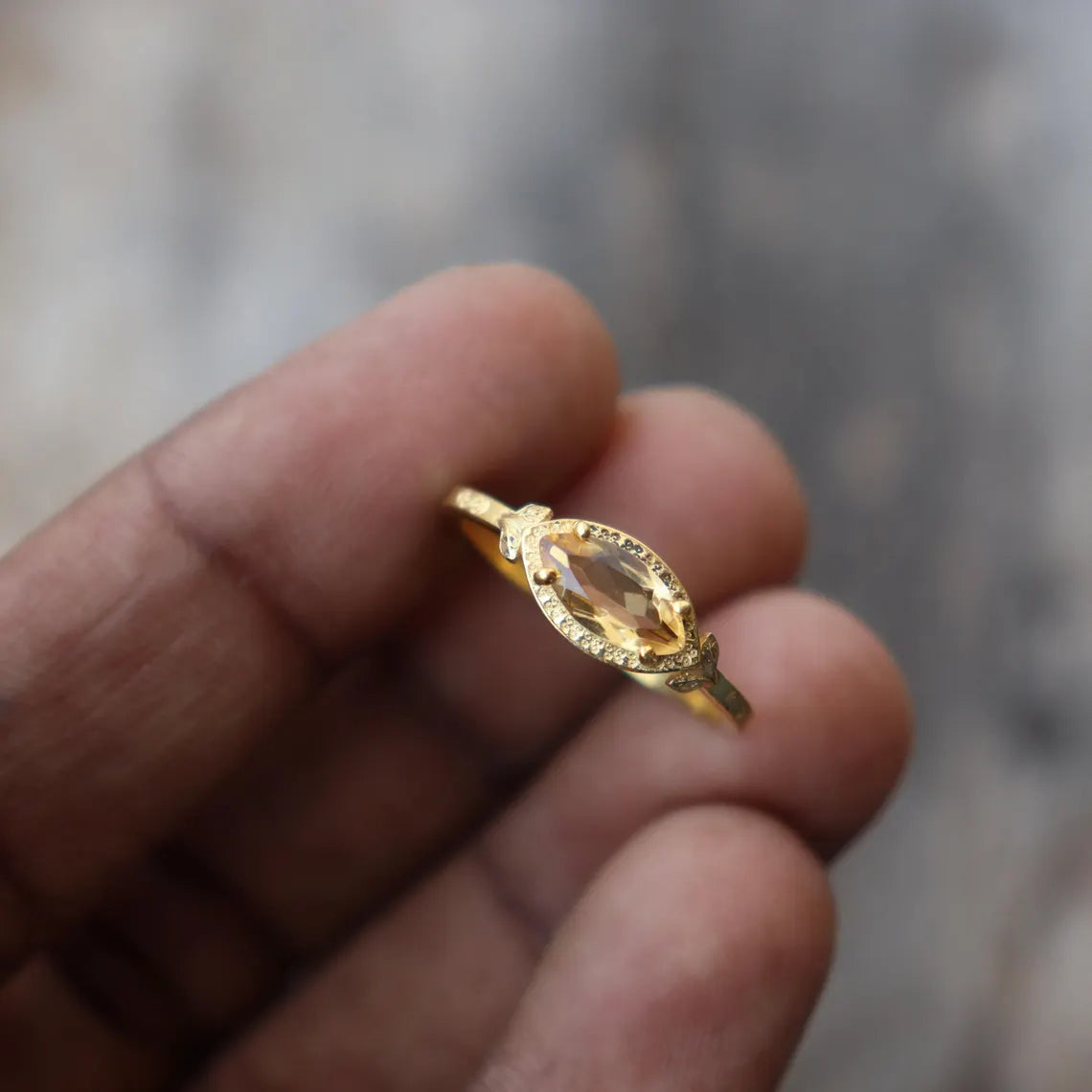 Gold ring with a clear gemstone held between fingers against a blurred background