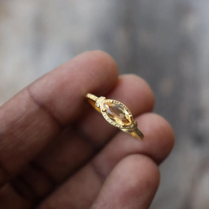 Gold ring with a clear gemstone held between fingers against a blurred background