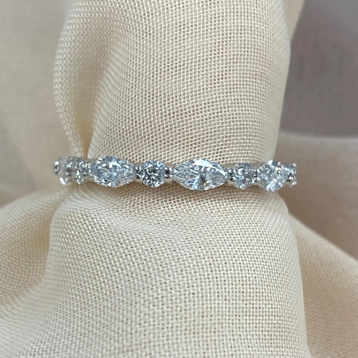 Silver ring with multiple diamonds on a beige fabric background