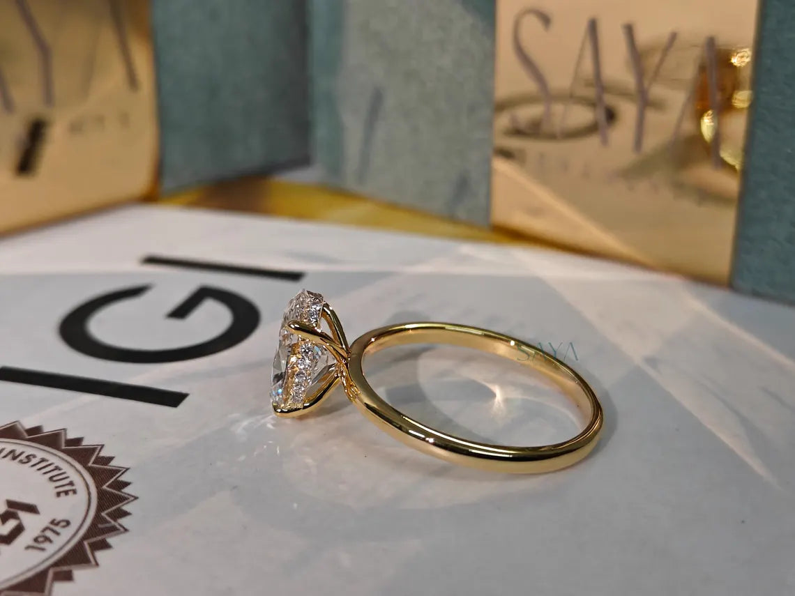 Gold ring with a diamond on a white surface with 'G' and 'SAY' visible