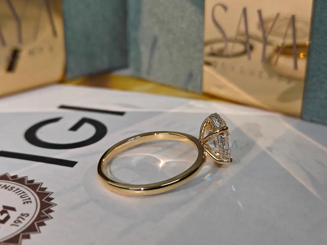 Gold ring with diamond on a white surface with 'Saya' branding in the background