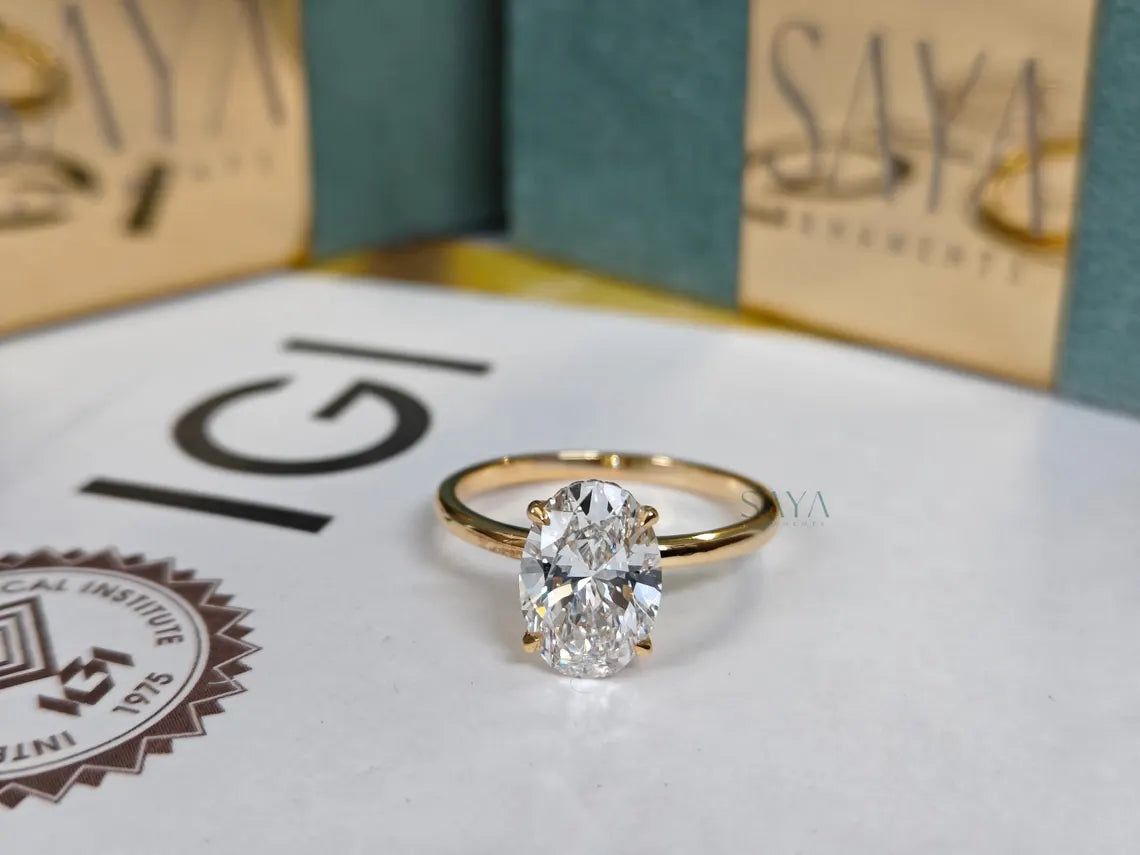 Gold ring with a diamond on a surface with 'IGI' and 'Saya' branding.