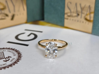 Gold ring with a diamond on a surface with 'IGI' and 'Saya' branding.