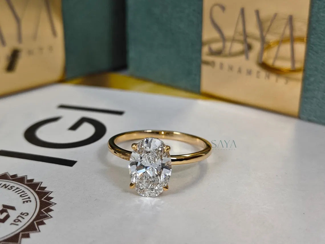 Gold ring with a diamond on a surface with 'Saya' and 'IGI' logos in the background.