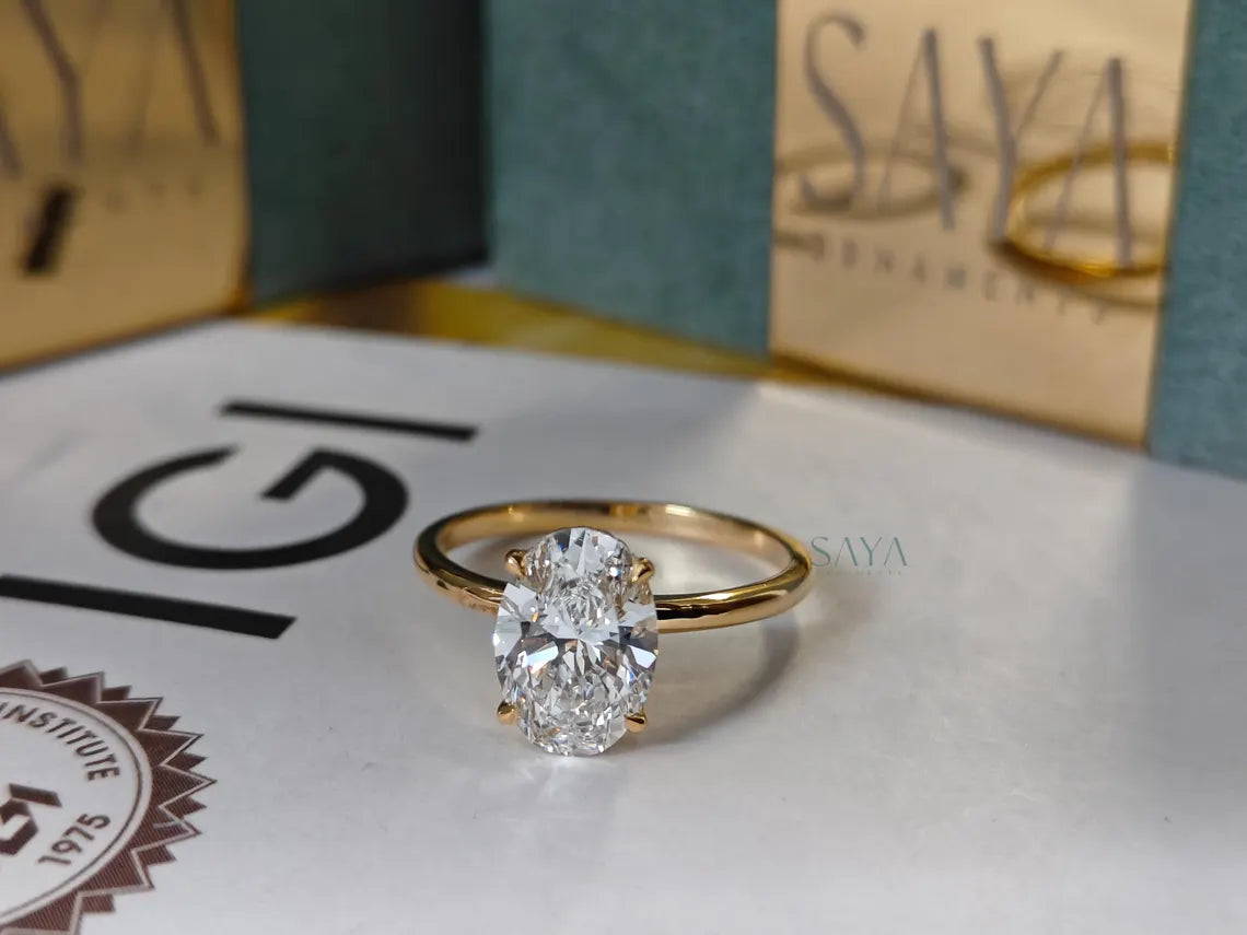 Gold ring with a diamond on a white surface with 'IGI' and 'Saya' branding.