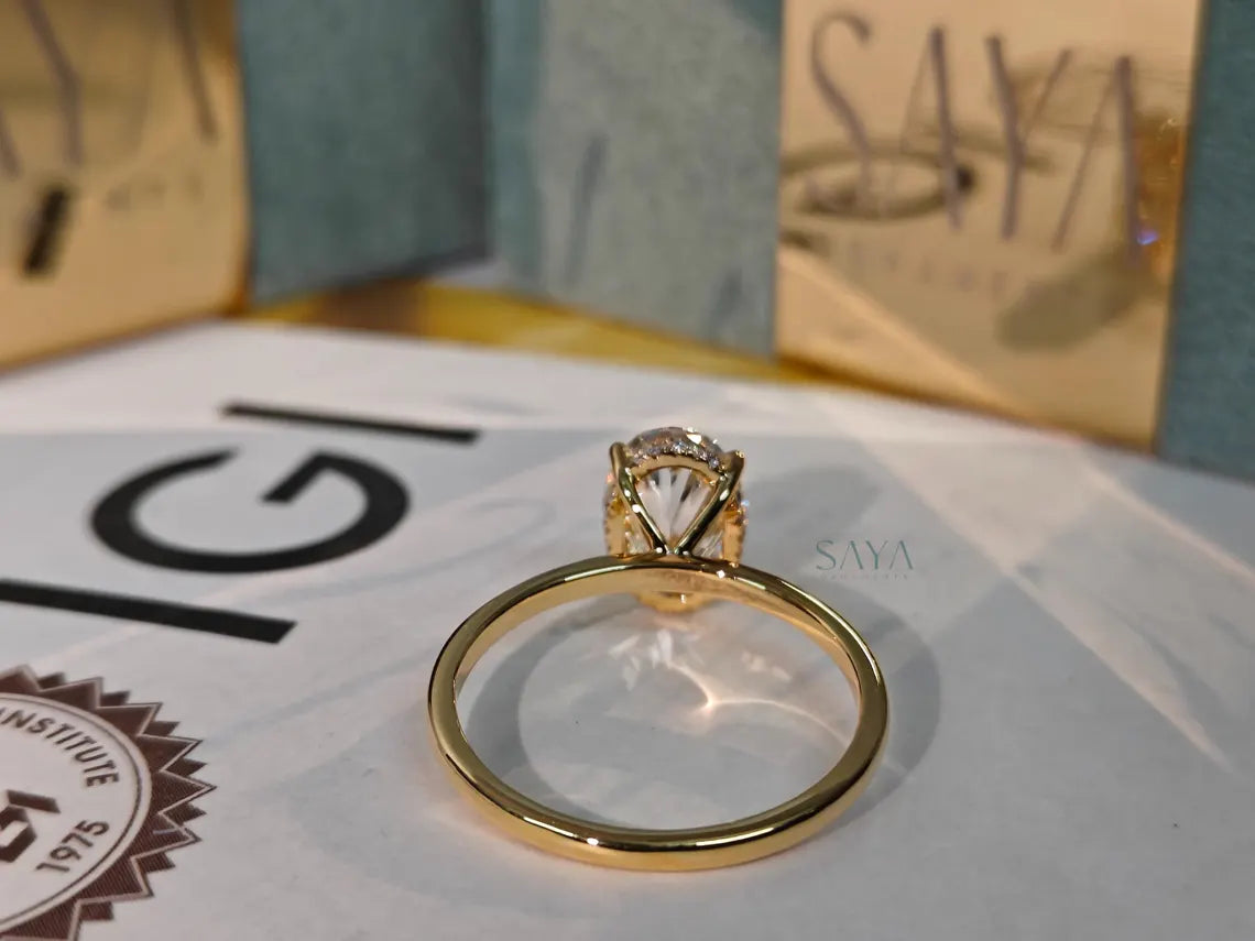 Gold ring with a diamond on a white surface with 'Saya' branding in the background.